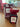 A red perfume bottle labeled #15 - Fine Trend from Dubai Essences is on a wooden surface. Behind it, the matching box with floral patterns echoes the design. Other products are blurred in the background.