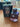 A #36 - Men More Intense by Dubai Essences bottle, featuring a dark cap and transparent body that hints at its purple scent, sits on a wooden surface next to its black and bronze packaging.